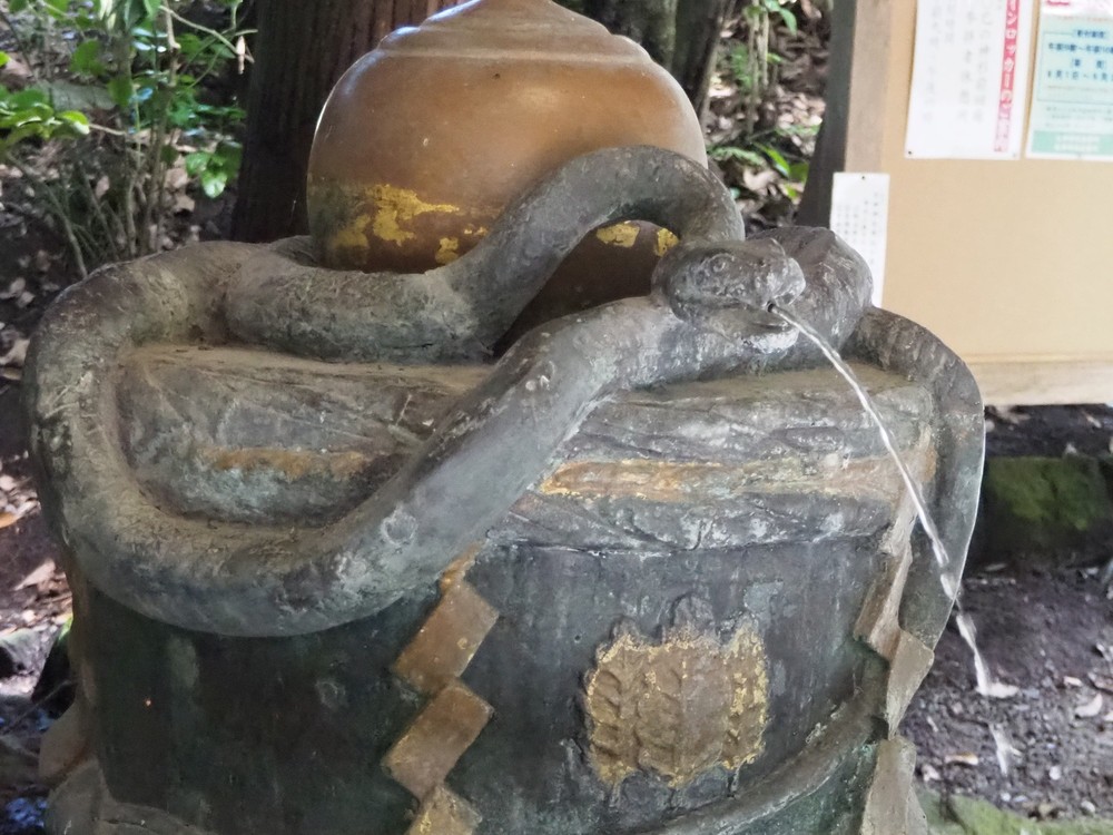 A bronze snake coiled around a sake jar pours sacred water at Omiwa Shrine