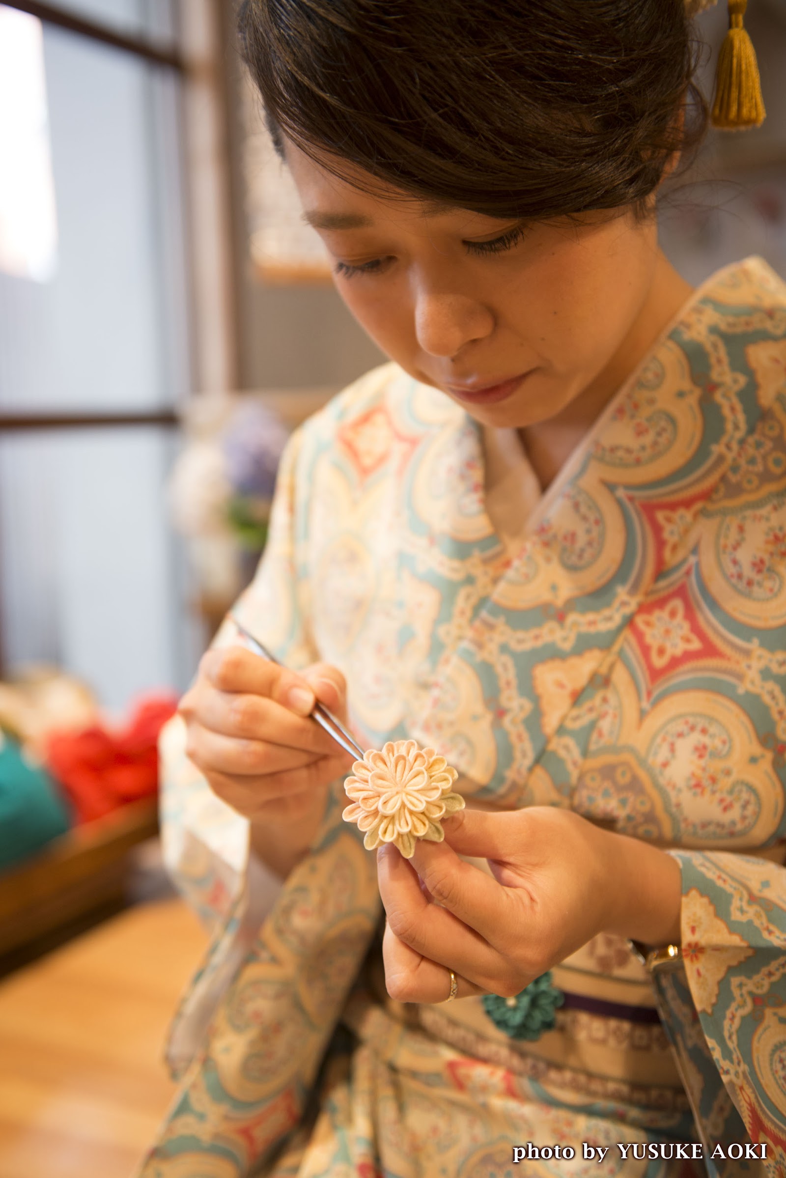 Tsumami zaiku artisan Ayano Fujii in kimono folding a chrysanthemum flower with tweezers