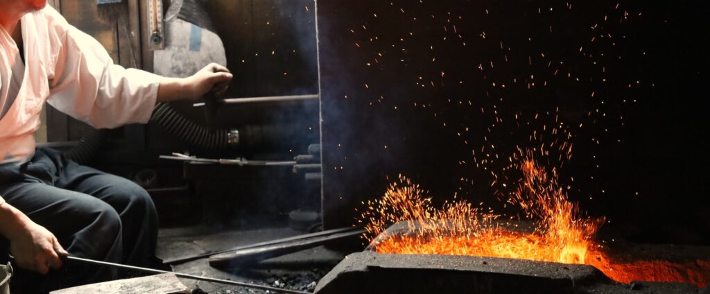 Seki swordsmith Kanetoki Kojima working steel at his forge as sparks rise from the fire