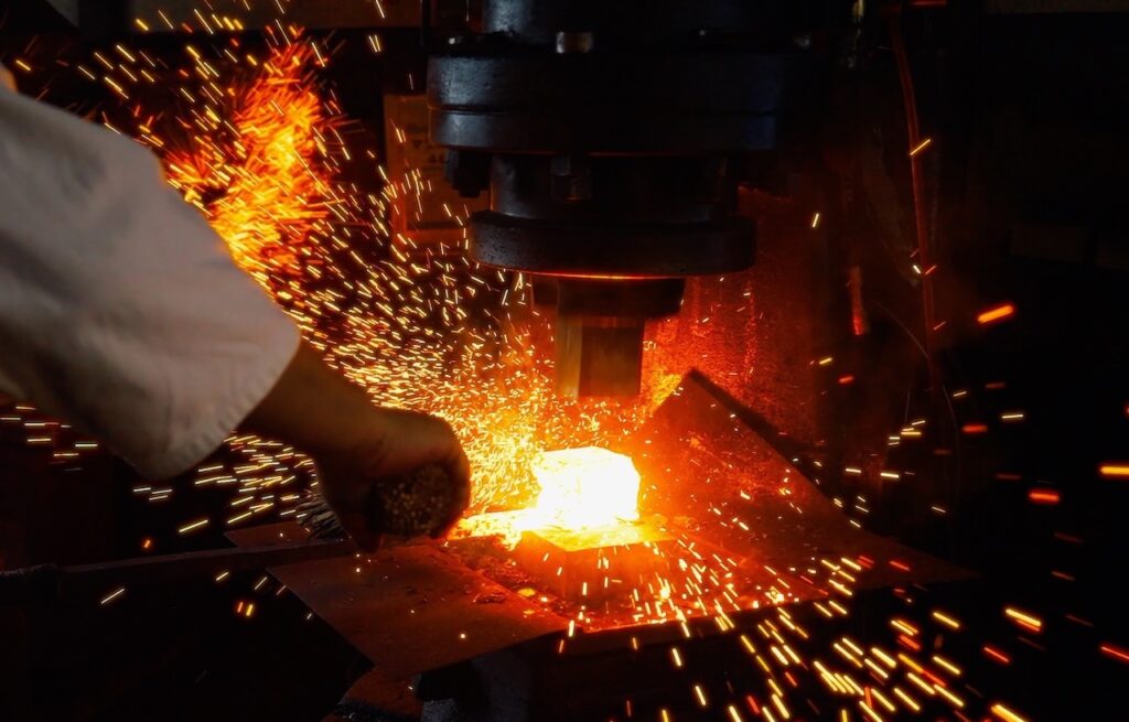 Sparks flying as glowing steel is worked under a power hammer in a Japanese forge