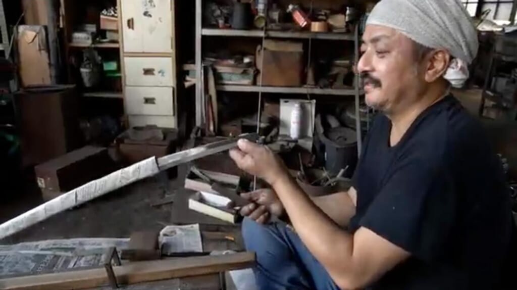 Swordsmith Kanetoki Kojima holding up an unpolished blade to check its line in his workshop in Seki